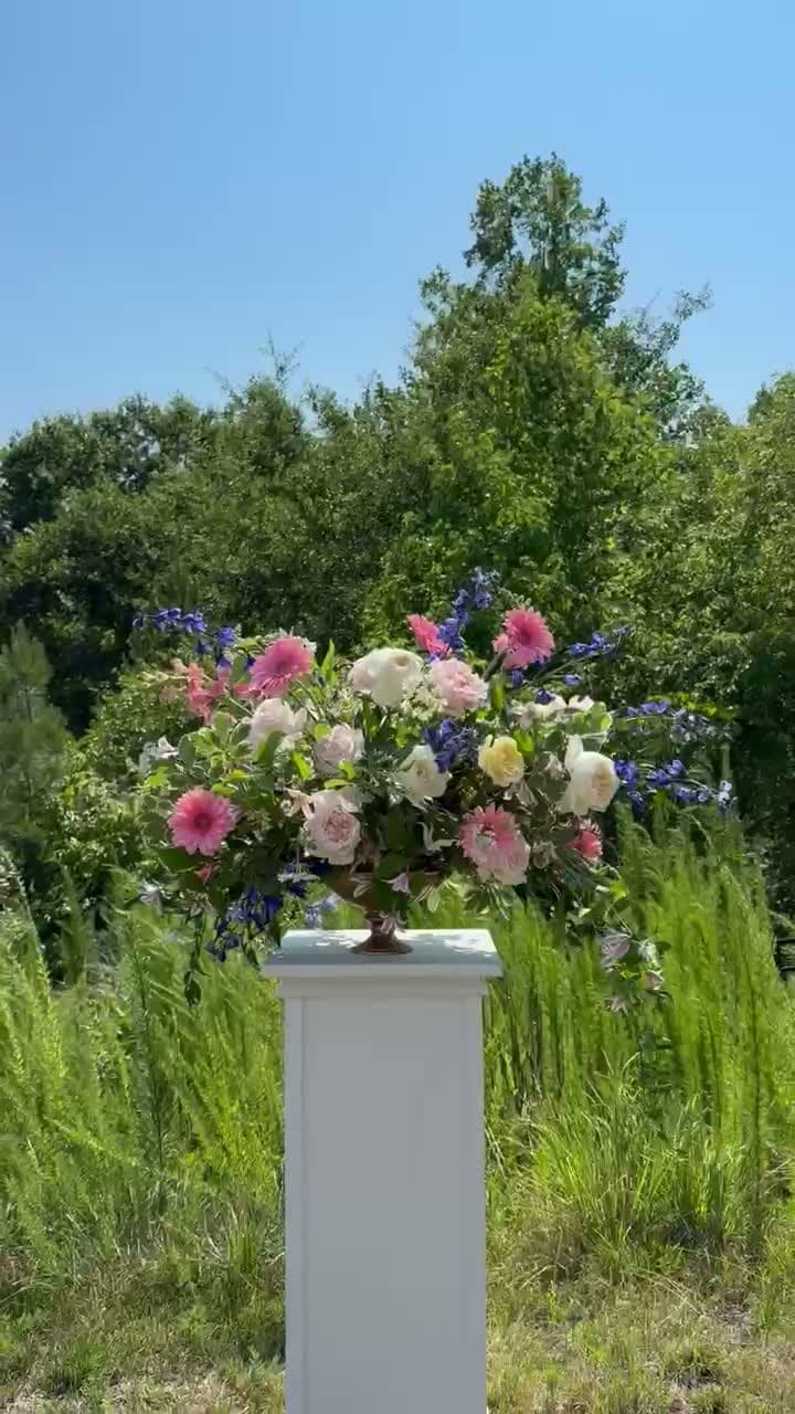 A large floral arrangement on a pedestal at an outdoor event